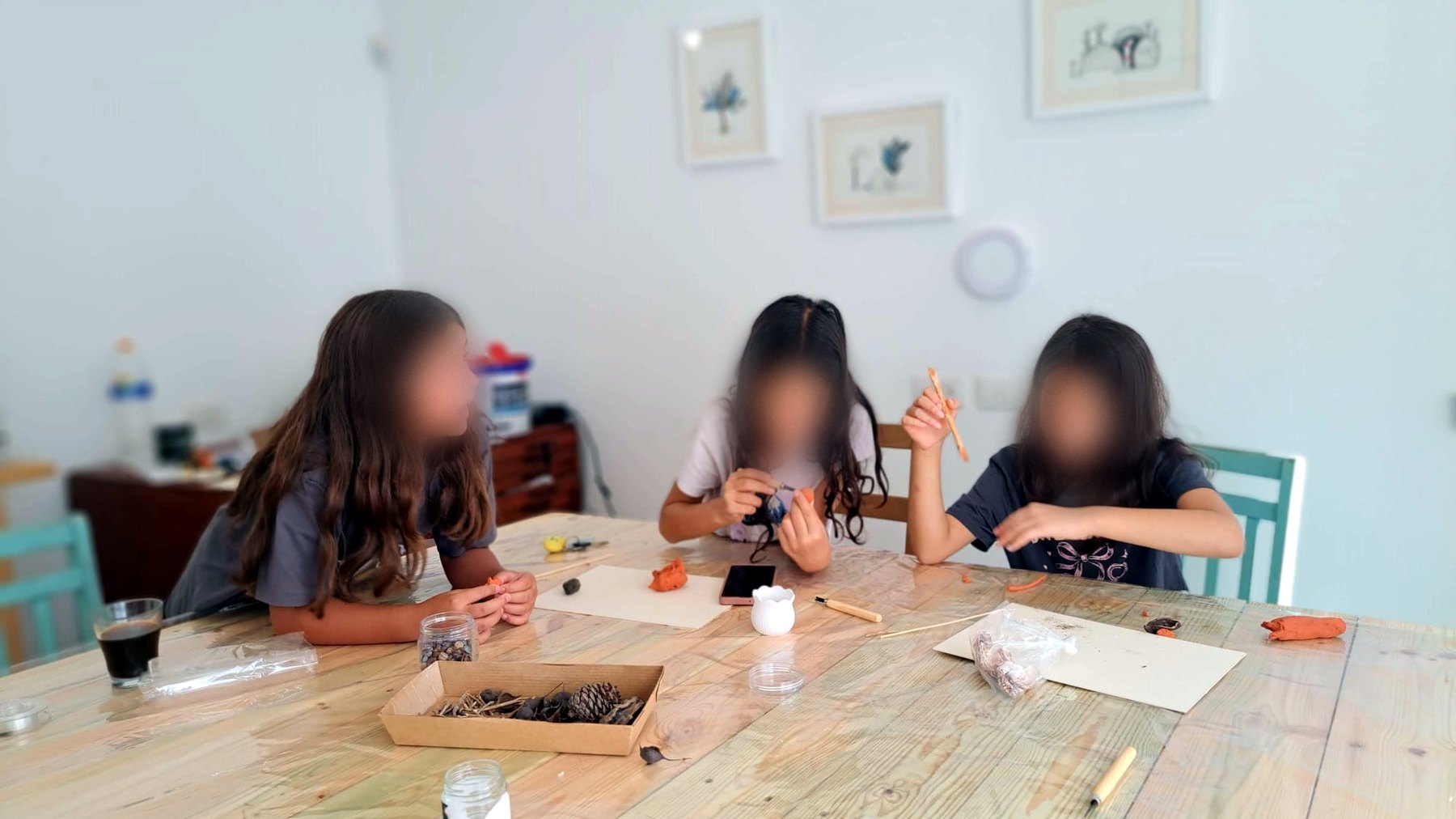 שלוש ילדות מעצבות בחימר ליד שולחן העץ