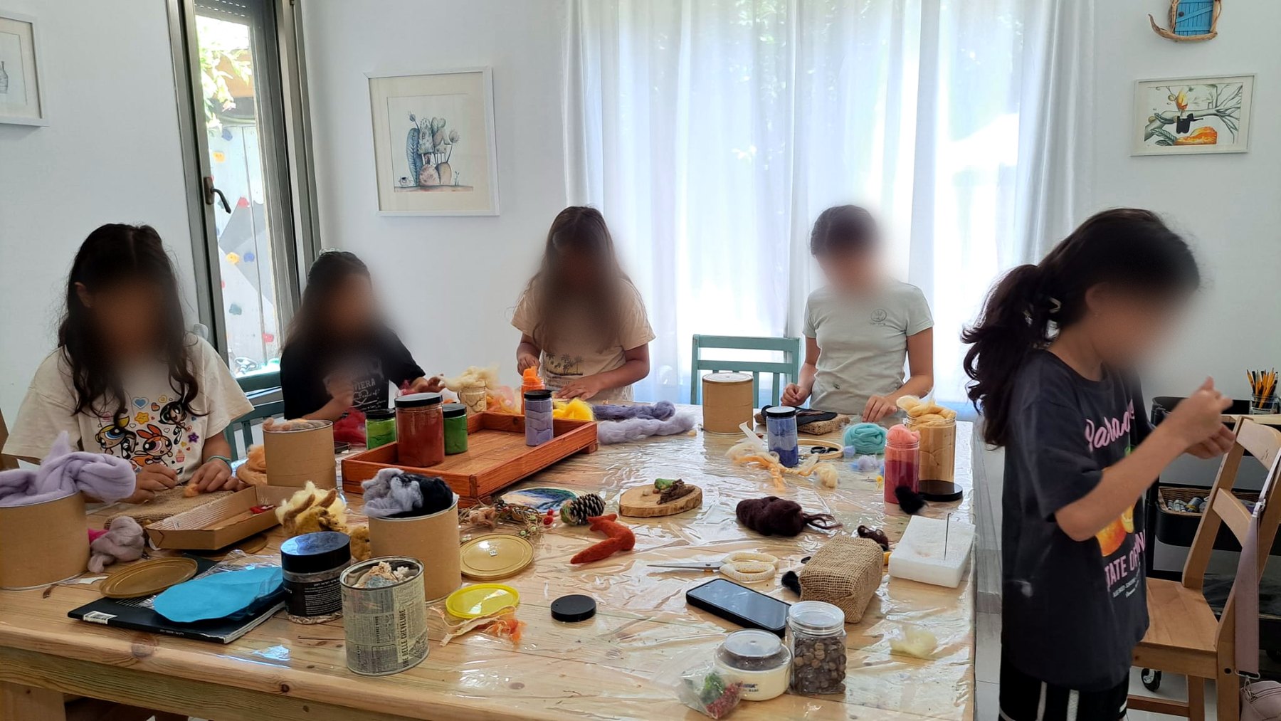 ילדות יוצרות סביב שולחן הסטודיו, עם צמר, צנצנות וחומרים